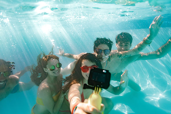 Eine fröhliche Gruppe junger Menschen lächelt unter Wasser in eine Actioncam
