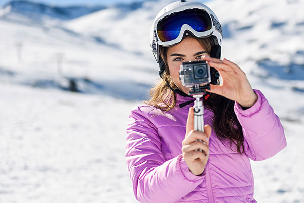 Eine Frau in Wintersport-Kleidung in einer verschneiten Landschaft hält eine Actioncam auf einem Gimbal