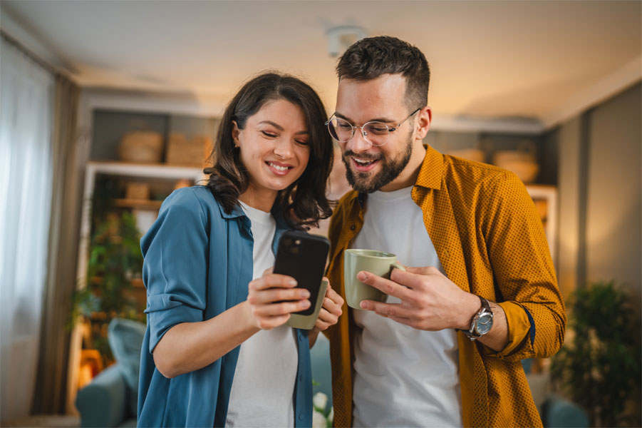 Eine Frau und ein Mann stehen nebeneinander und blicken gemeinsam fröhlich auf ein Smartphone